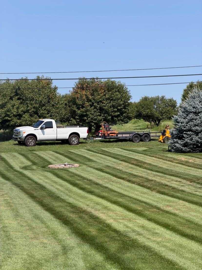 White pickup truck and equipment trailer on a freshly mowed lawn with tree lines.