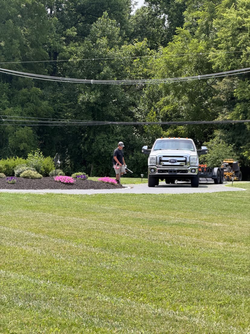 Man landscaping near a truck, with pink flowers and green grass in background.