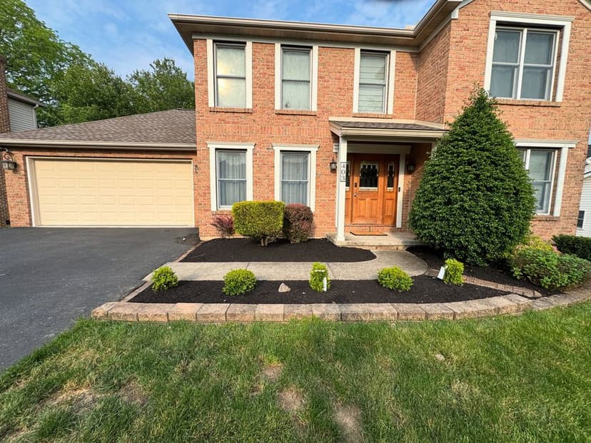 Brick home with landscaped front yard and garage, highlighting neat shrubs and fresh mulch.